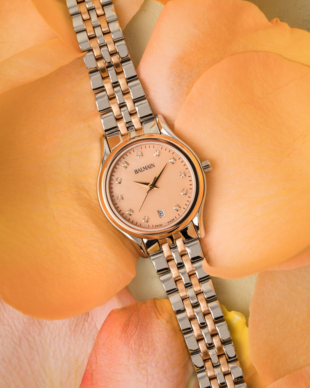 Gros plan sur une montre Balmain Beleganza avec cadran Peach Fuzz, aiguilles Dauphine et flanc de bo&icirc;tier grav&eacute;.