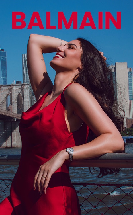 Frau in einem roten Kleid, die eine Balmain-Uhr tr&auml;gt, w&auml;hrend sie auf einer Stra&szlig;e in New York City steht.