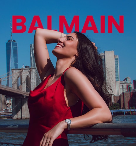 Woman in a red dress wearing a Balmain watch while standing in a New York City street.