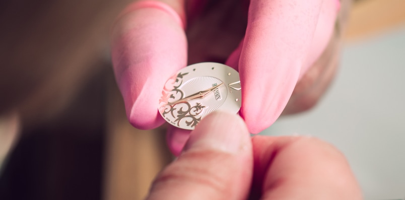 Elegant arabesque motifs and diamond embellishments inspired by Parisian Haute Couture Close-up of a watchmaker assembling a Balmain watch, highlighting Swiss craftsmanship